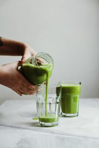 person holding clear drinking glass with green liquid - ways to make celery juice
