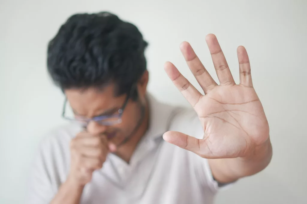 a man holding his hand up in front of his face, cough