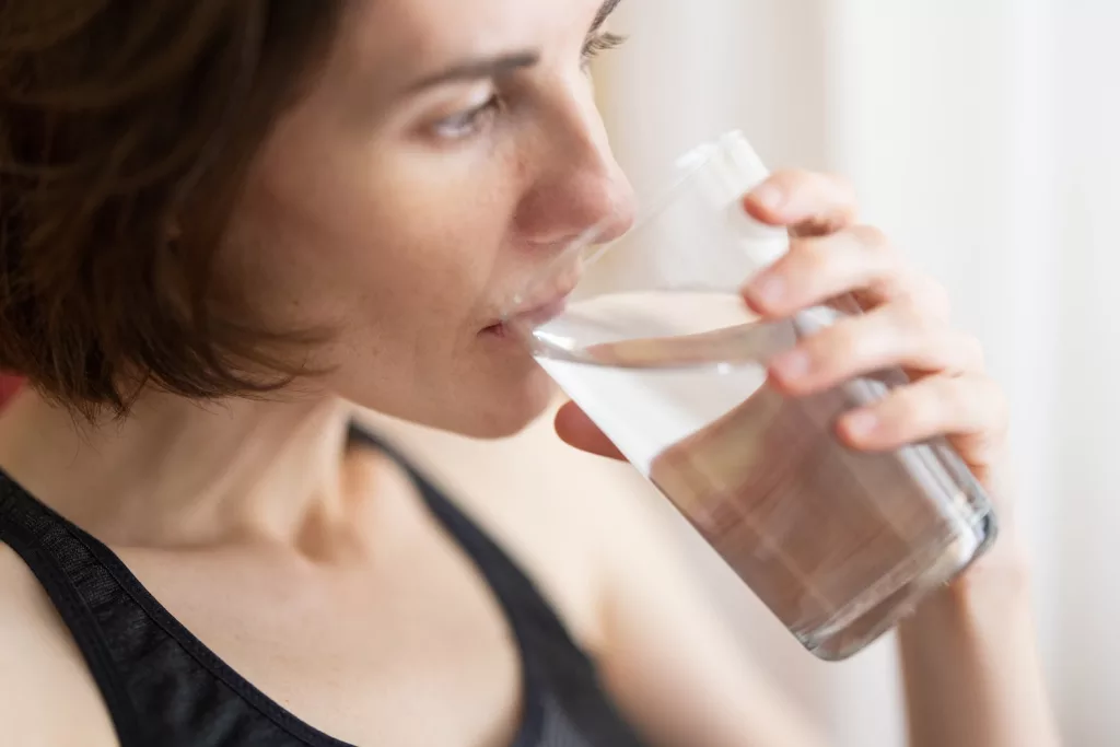 woman in black tank top drinking water, cough remedies you can make at home