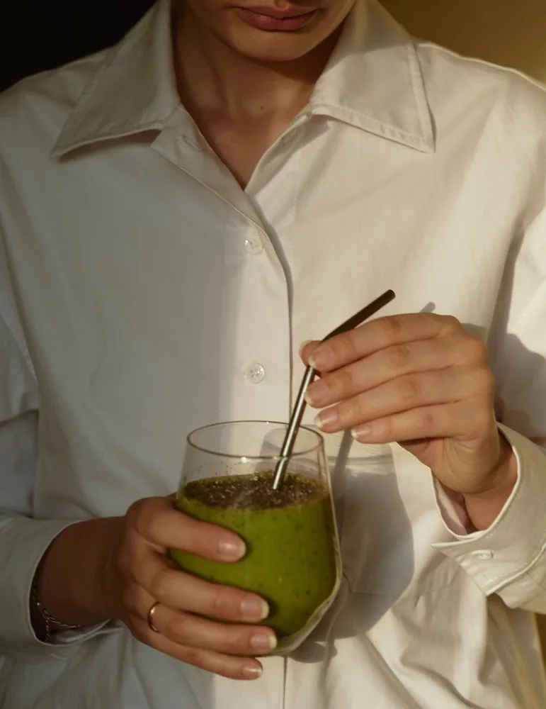 matcha's health benefits, person in white button up shirt holding clear drinking glass with green liquid