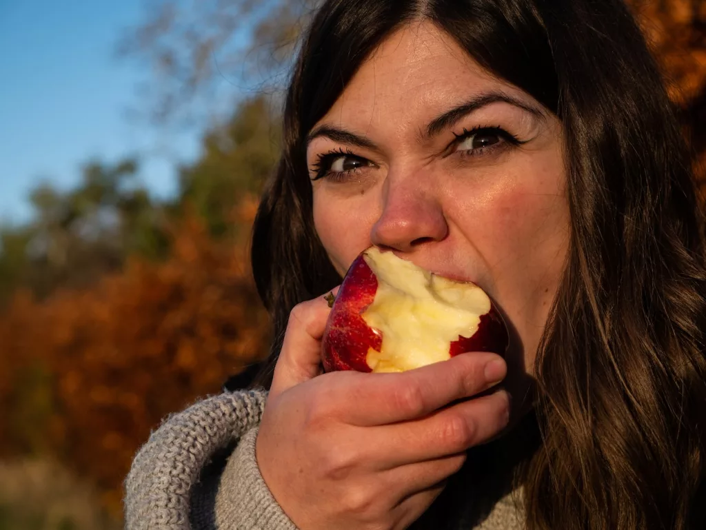 woman in gray sweater holding sliced of apple, one of the tips to prevent digestive problems is by eating apples