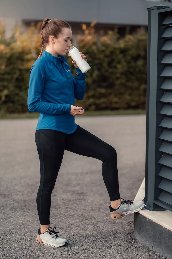 a woman in a blue jacket drinking from a cup, drink plenty of water - healthy eating habits