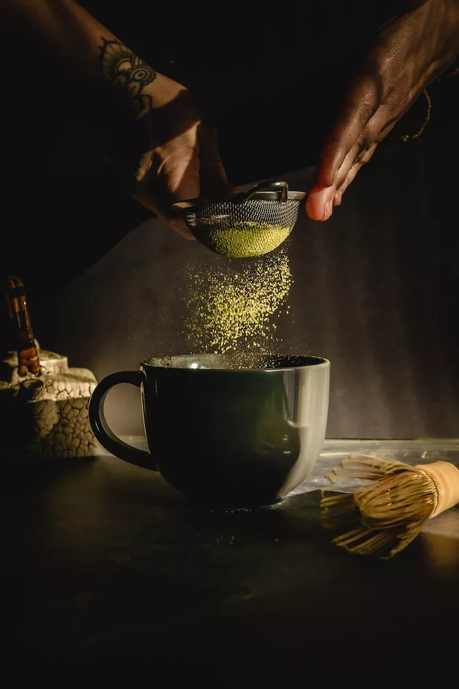 person pouring water on black ceramic mug, matcha, origin of matcha