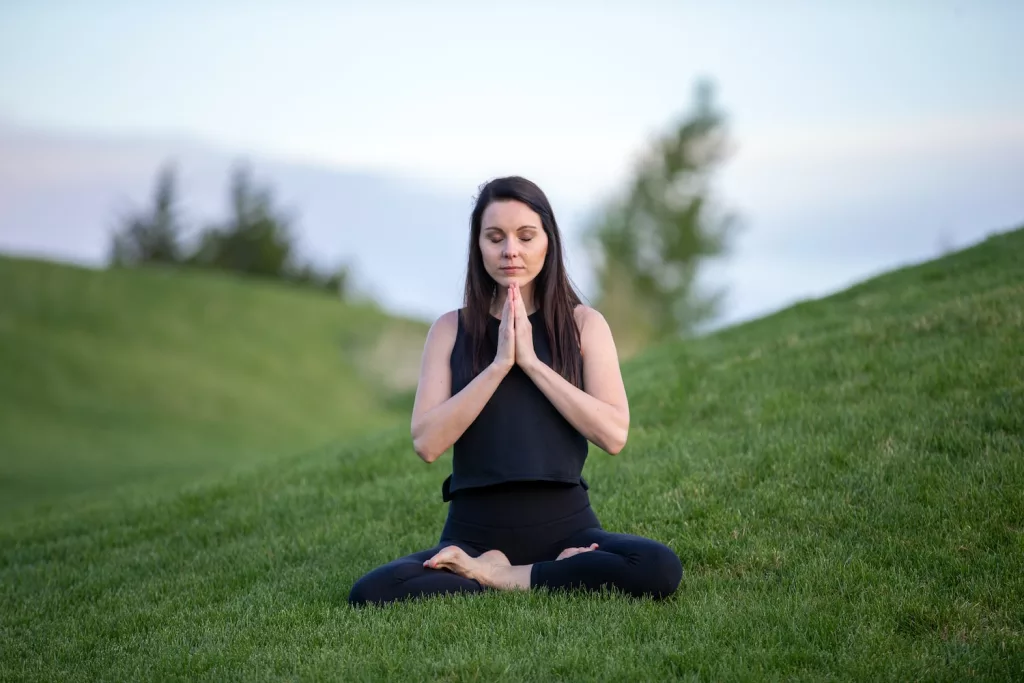 woman in black tank top and black pants sitting on green grass field during daytime, natural remedies for stress relief