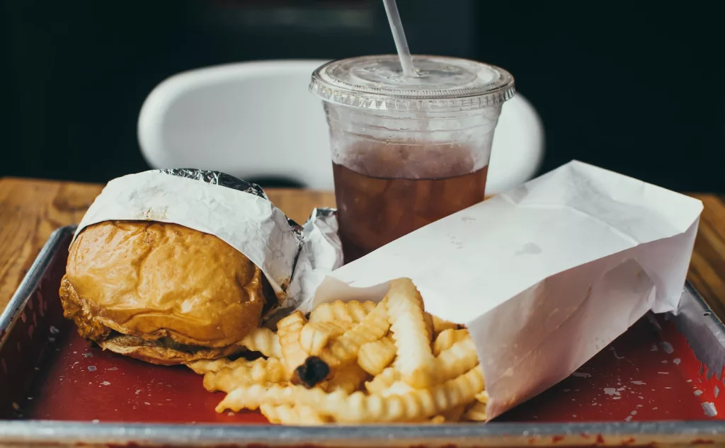 burger beside fried potatoes with drinking glass, certain foods causes heartburn