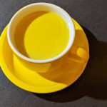 a cup of tea sits on a yellow saucer | turmeric milk recipe for cold and cough